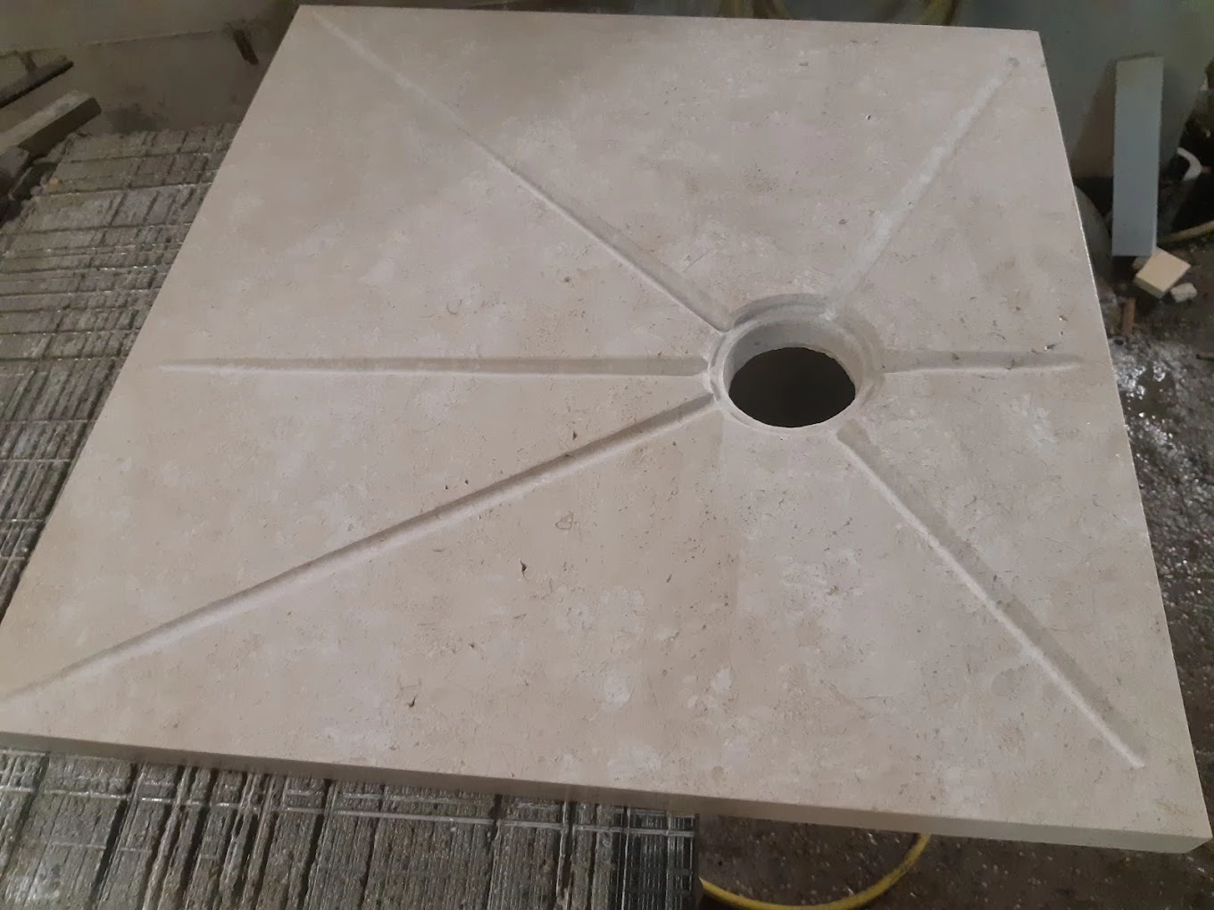 Piatto doccia in pietra beige con scanalature a raggiera verso lo scarico, lavorato da Marmeria Deidda